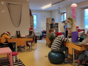 Salle de classe festive avec élèves en bonnets de Noël, concentrés à leurs bureaux.