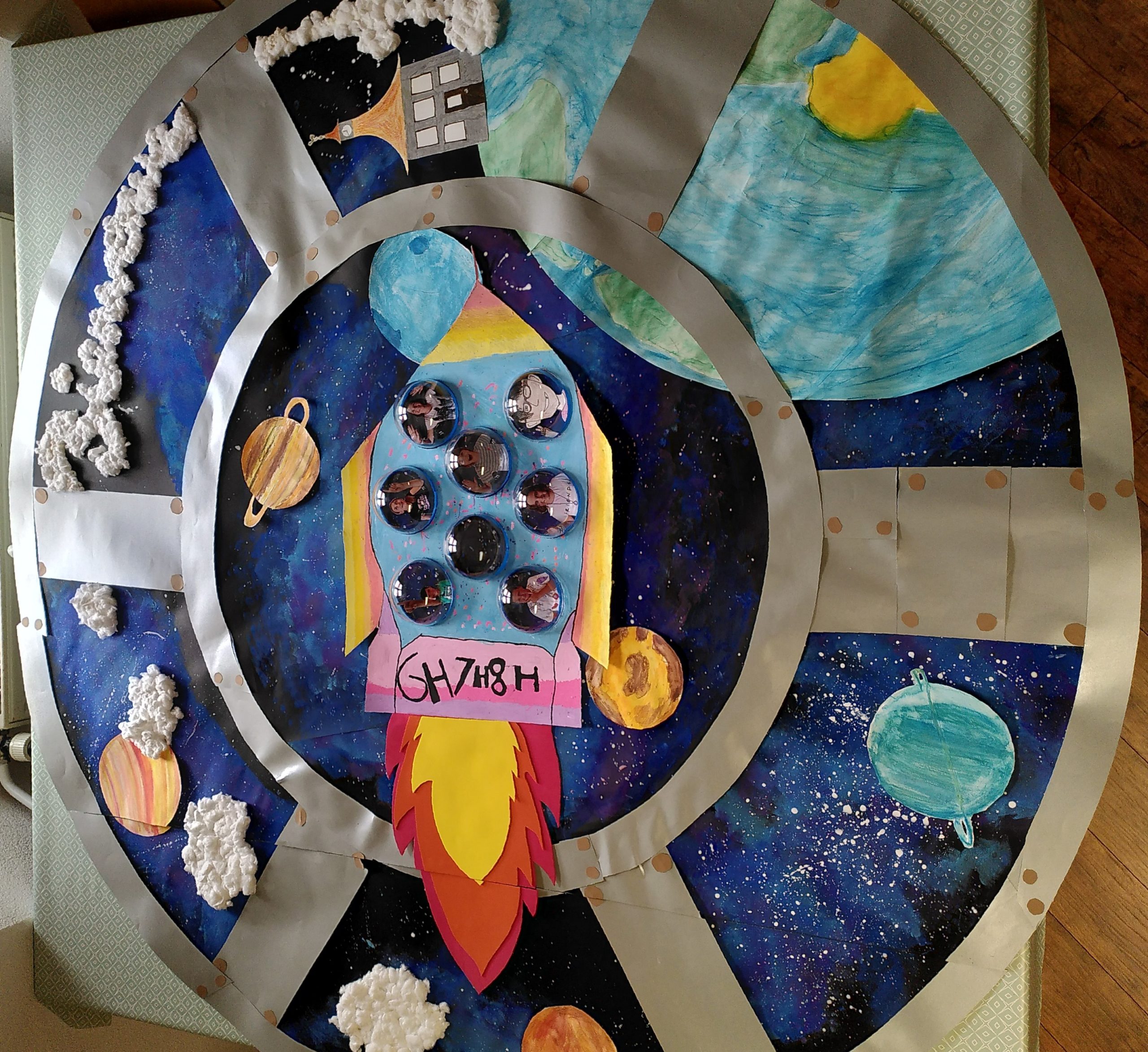 Maquette spatiale avec fusée colorée, nuages en coton, fond étoilé et planètes dessinées.